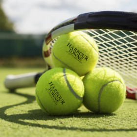 Lifestyle photo of Harbourtowne at Countrywoods branded tennis balls under tennis raquet Lifestyle photo of Harbourtowne at Countrywoods branded tennis balls under tennis raquet